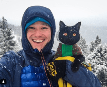 man and his black cat camping in the snow