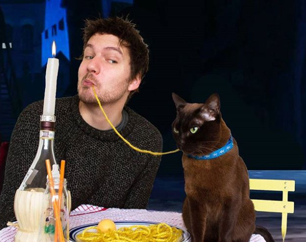 man and black cat share a string of spaghetti